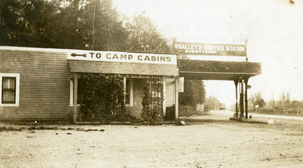 Side view of Whalley’s Service Station showing a sign pointing to camp cabins